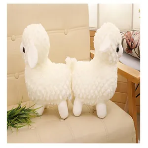 Detail view of two fluffy white sheep plush toys sitting on a cozy beige chair in a home setting.