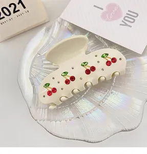 Close-up of elegant cream acetate hair claw clip with red rhinestone cherry patterns