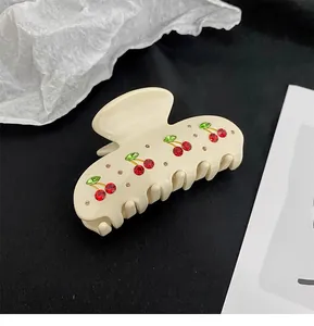 Detail view of a French cream acetate hair claw clip with rhinestone cherry patterns