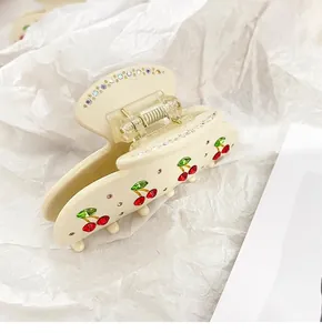 Detailed macro view of cream acetate hair claw clip featuring elegant cherry rhinestones