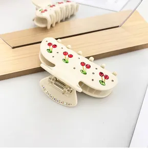 Close-up detail of cherry rhinestone patterns on an elegant cream acetate hair claw clip.