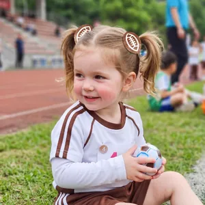 Petite fille portant des pinces à cheveux football américain marron pailletées au sport