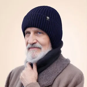 An elderly man wearing a dark blue thick knitted winter beanie with a snowflake logo tag.