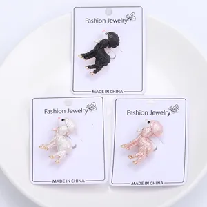 Three cute poodle enamel brooches in black, white, and pink displayed on jewelry cards