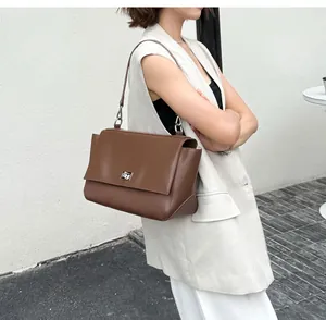 Stylish model wearing a brown leather messenger bag with flap and metal lock closure