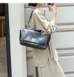 Stylish black leather flap messenger bag with silver lock carried by a model in city
