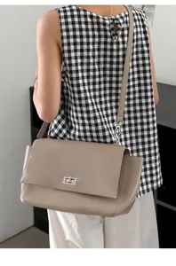 Detailed view of a stylish taupe leather messenger bag with flap and metal lock closure