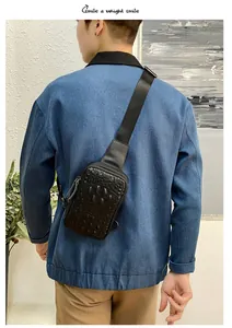 Détail montrant un sac de poitrine en cuir noir motif crocodile sur une veste en jean