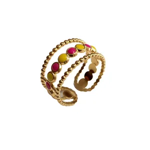 Dettaglio di un anello aperto in acciaio dorato con punti in smalto rosa e giallo.