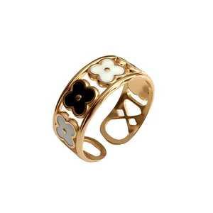 Dettaglio anello aperto in acciaio dorato con fiori in smalto bianco e nero.