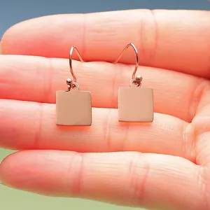 Detailed view of rose gold square stainless steel mirror earrings held in a palm