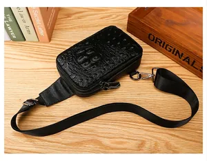 Sac de poitrine en cuir noir avec motif crocodile pour homme, posé à plat sur table.