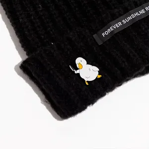 Macro detail of a funny white duck enamel pin with a knife on black knit fabric