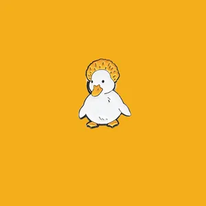 Close-up macro view of a cute white duck enamel pin with an orange crown on yellow backdrop