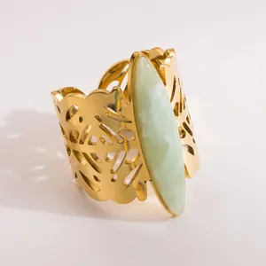 Detail of a wide gold stainless steel open ring with marquise green stone and leaf cutout.