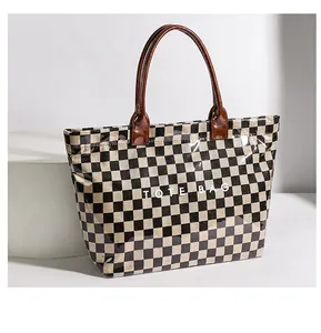 Detailed view of the checkered tote bag featuring a glossy PVC finish and brown handles