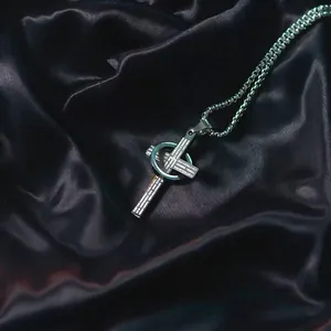 Close-up of stainless steel cross necklace with engraved text and circular ring detail.