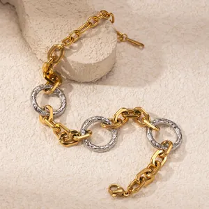 Primo piano di un bracciale a catena spessa color oro e argento su una pietra ruvida.