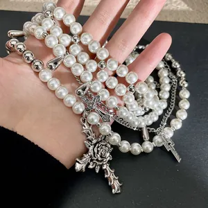 Hand holding multi-layer pearl necklace with ornate silver cross and rose charms