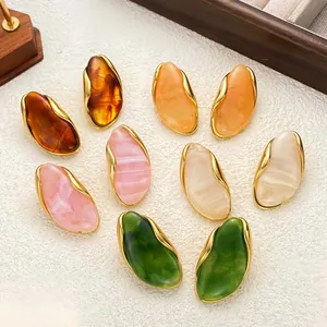 Macro view of colorful irregular resin stud earrings with gold trim on white background