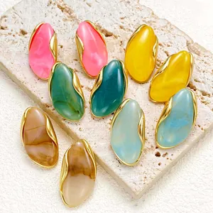 Multi-colored irregular resin stud earrings with golden frames on textured stone