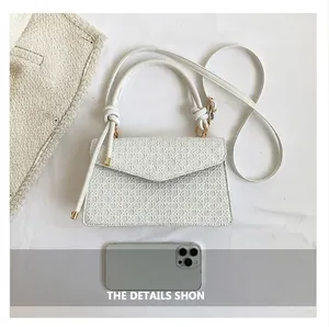 Close-up detail of a white textured retro handbag with knot handle and long strap