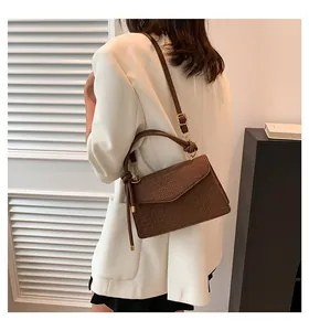 Stylish brown textured crossbody bag with gold hardware worn with a white blazer