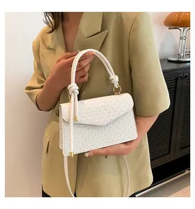 Elegant white crossbody bag with woven texture and gold hardware, held by a model.
