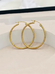 Detailed close-up view of large gold hoop earrings with elegant textured stripe pattern
