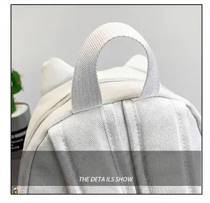 Close-up detail showing the durable woven top handle of a white cat-eared canvas backpack