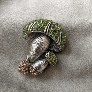 Vintage silver mushroom brooch with green and champagne rhinestones on grey fabric