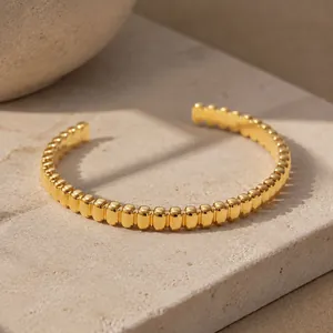 Close-up view of a gold-plated stainless steel cuff bracelet with beaded texture.