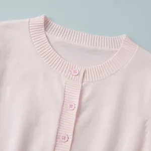 Dettaglio ravvicinato del collo a coste e dei bottoni rosa su un cardigan in maglia