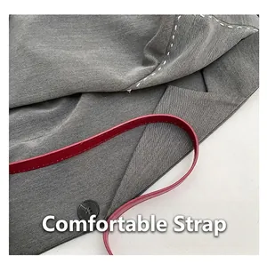Detail of gray fabric tote bag with slim red shoulder strap and white stitching