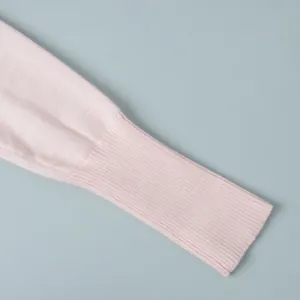 Dettaglio della manica di un cardigan in maglia rosa con polsino a costine fini.
