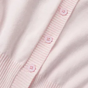 Dettaglio macro di un cardigan in maglia rosa con bottoni coordinati e abbottonatura