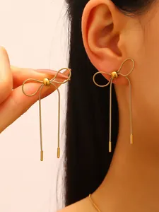 Detailed close-up of gold stainless steel bow tassel earrings shown on model's ear