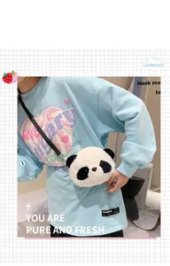 Close-up of a cute panda plush crossbody bag worn over a stylish light blue sweatshirt.