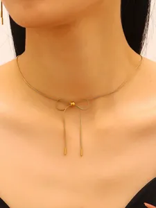 Detailed close-up of a gold stainless steel bow pendant necklace on a model's neck.