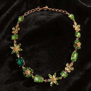 Détail du collier fleurs en pierres vertes vintage sur fond de velours noir élégant.