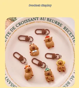 Collection of five cute cartoon Capybara resin keychains shown on a decorative plate.