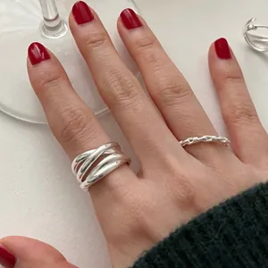 Detailed view of silver irregular crisscross rings worn on hand with red nails.