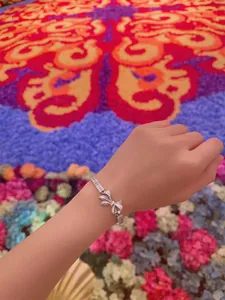 Elegant silver ribbon bow bracelet with sparkling pavé-set stones shown on a wrist.