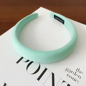 Détail d'un serre-tête rembourré vert menthe posé sur un magazine de mode.