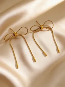Close-up detail of elegant gold-toned stainless steel bow drop earrings on satin