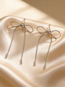 Elegant silver stainless steel bow earrings with long drop tassels on satin background