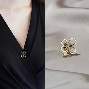 Detail view of a golden four-leaf clover safety pin on elegant grey satin fabric.