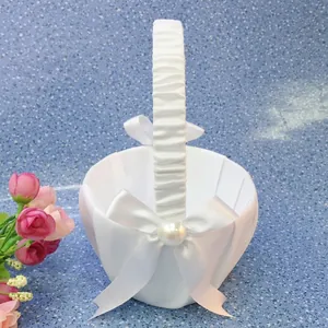 Detail of a white satin flower girl basket with a pearl-accented bow for weddings.