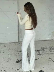 Vista laterale a figura intera di una donna con top in maglia e pantaloni bianchi eleganti