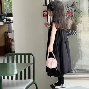 Niña con vestido negro y un mini bolso redondo rosa de cuero sintético